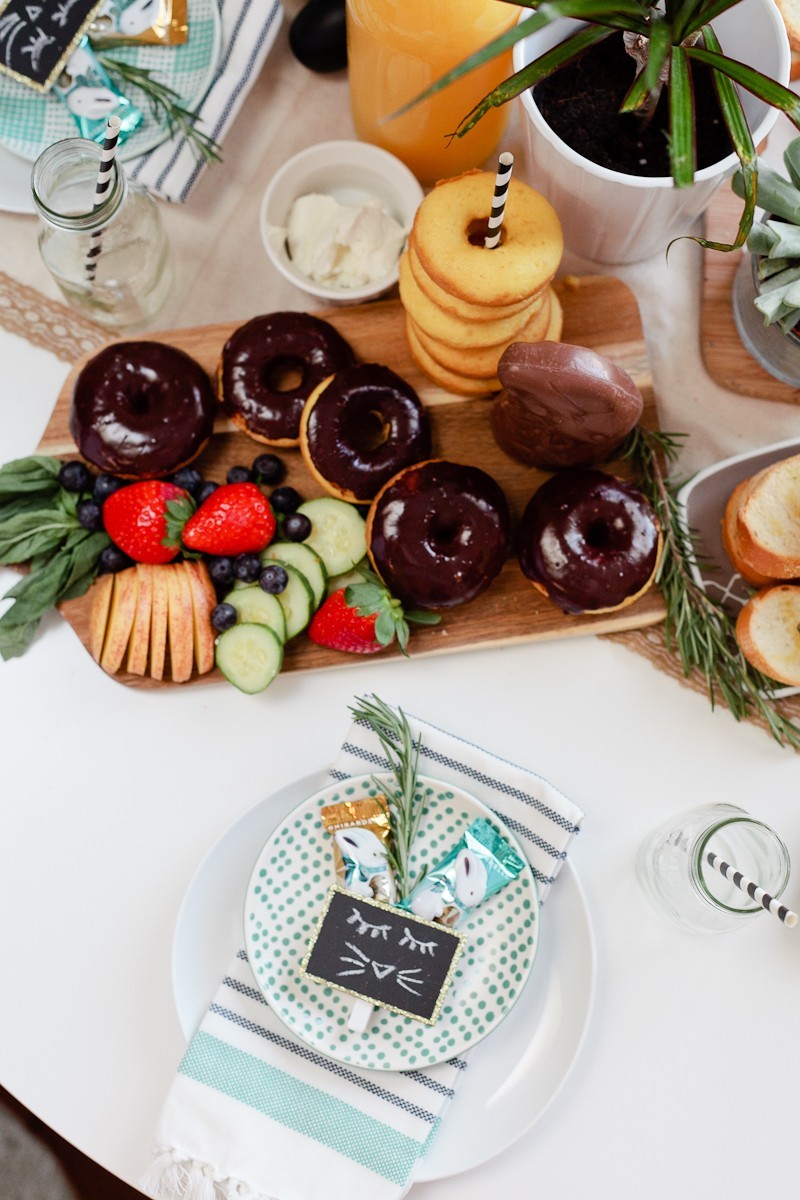 easter brunch ideas |Easter Brunch Ideas by popular Florida lifestyle blog, Fresh Mommy Blog: image of a wooden cutting board filled with cucumber slices, strawberries, blueberries, glazed donuts, chocolate frosted donuts, and a chocolate bunny. 