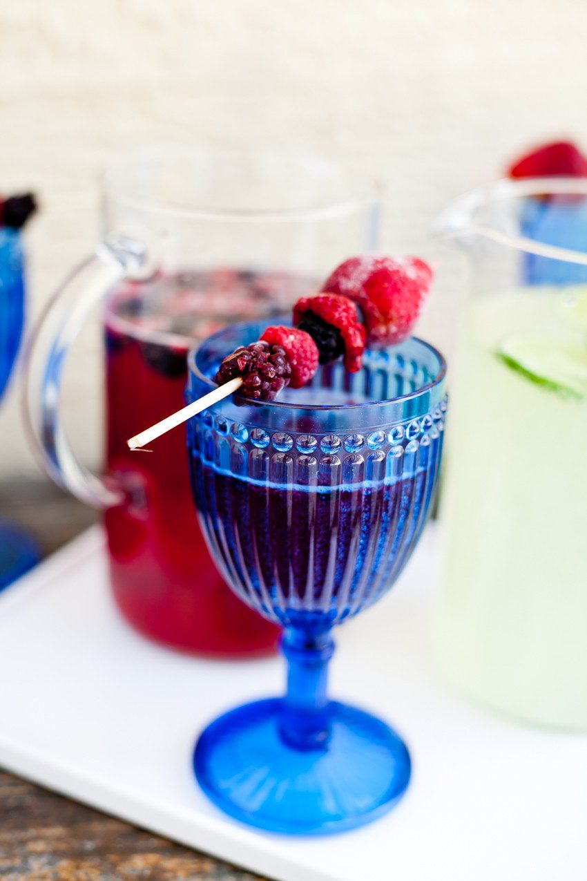 Sparkling Party Punch. Make it two ways... a sparkling red berry punch or sparkling limeade for the perfect summer party drink. Top with frozen berries for a festive touch... Memorial Day, July 4th, red white and blue drinks! | Grilling Season by popular Florida lifestyle blog, Fresh Mommy Blog: image of a cocktail drink in a vintage blue glass with a berry kabob resting across the top of the cup. 