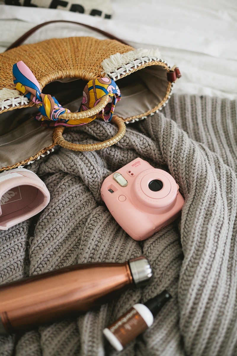 Road Trip Essentials and The Ultimate Road Trip Playlist with music for a happy, adventurous trip. - Travel Essentials: The Ultimate Road Trip Playlist by popular Florida lifestyle blogger Fresh Mommy Blog | Family Road Trip Playlist by popular Florida travel blog, Fresh Mommy Blog: image of a woven handbag, pink polaroid camera, grey knit blanket, and pink Vans sneakers. 