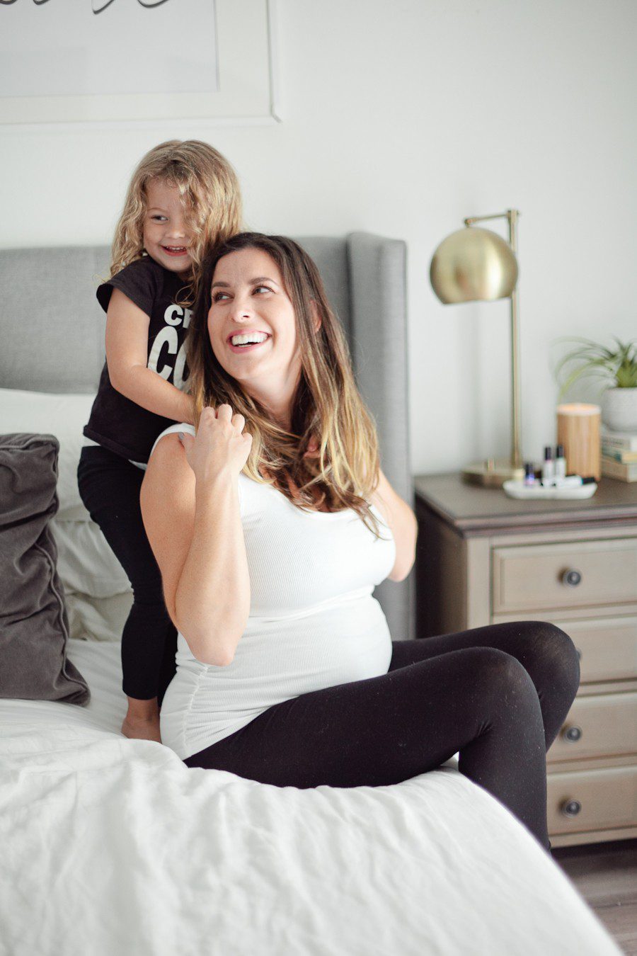 My First Trimester Survival Guide: Tips and Favorites | First Trimester Pregnancy Essentials: An Early Pregnancy Survival Guide by popular Florida lifestyle blog, Fresh Mommy Blog: image of a mom sitting on her bed with her daughter standing behind her and wrapping her arms around her.