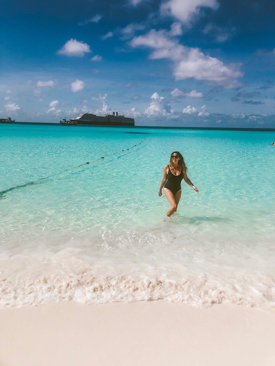 5 Amazing Reason to go on a Holland America cruise with Oprah Magazine by popular US lifestyle blog Fresh Mommy Blog: image of woman wearing a black one piece swimsuit and standing in the Caribbean ocean with a Holland America cruise ship on the horizon. 
