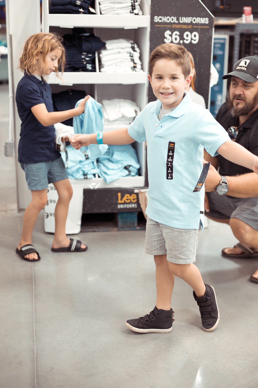5 Sensational Strategies to Make Getting Ready for School Easy | How to Get Ready for School: 5 Sensational Strategies to Make Easy on your Family by popular Tampa life and style blog, Fresh Mommy: image of a dad helping his two young sons try on a blue Lee polo shirt.