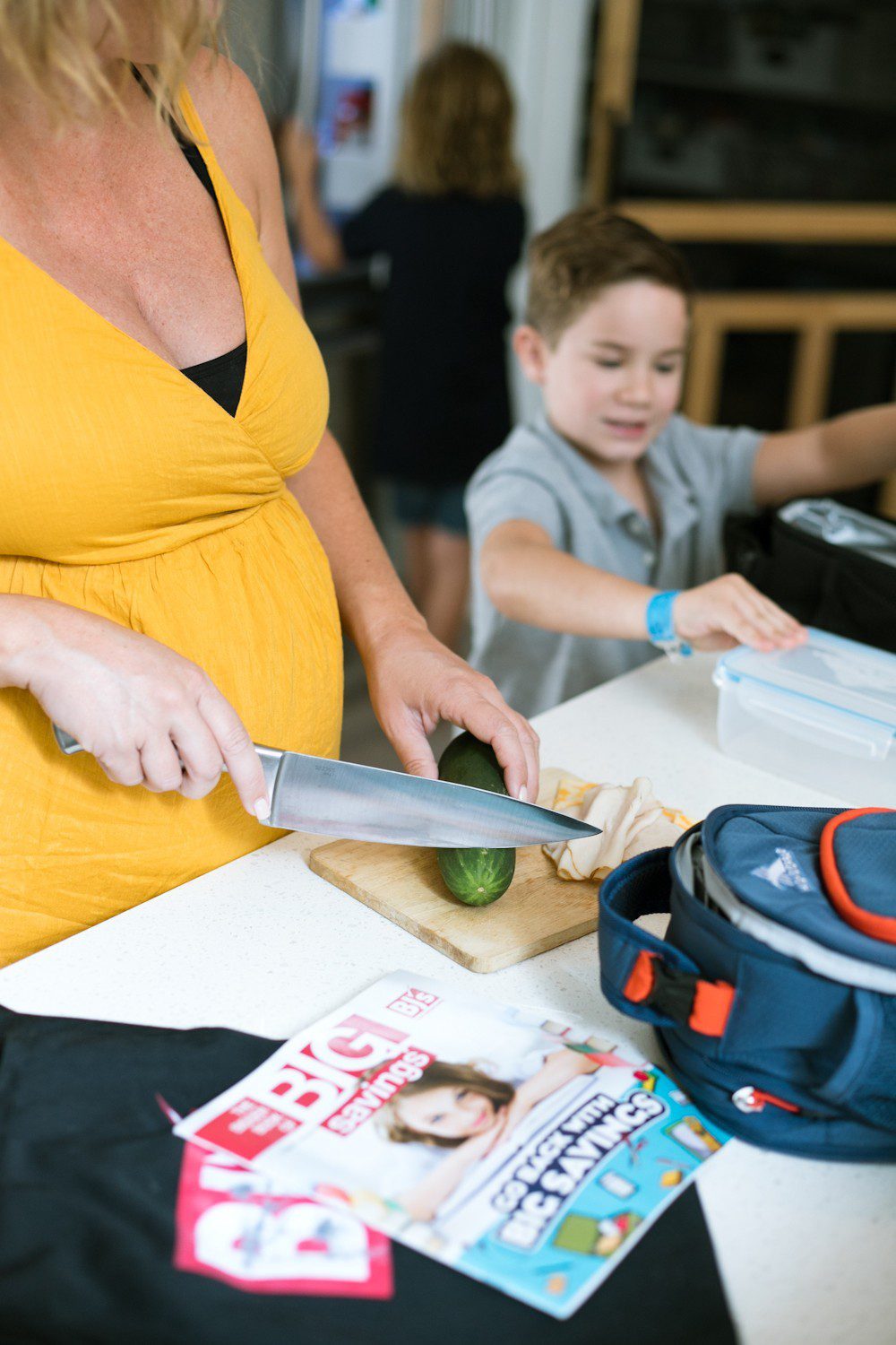 5 Sensational Strategies to Make Getting Ready for School Easy | How to Get Ready for School: 5 Sensational Strategies to Make Easy on your Family by popular Tampa life and style blog, Fresh Mommy: image of a woman standing her kitchen cutting a cucumber while her kids pack things into their lunch bags.