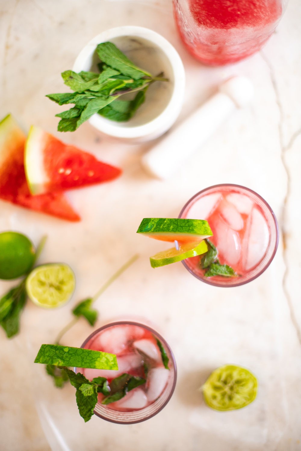 Refreshingly Easy Summer Mocktail Recipes including this hydrating watermelon mojito mocktail by popular Florida lifestyle blog, Fresh Mommy: image of Watermelon mojiotos on a marble countertop surrounded by lime halves and watermelon slices.