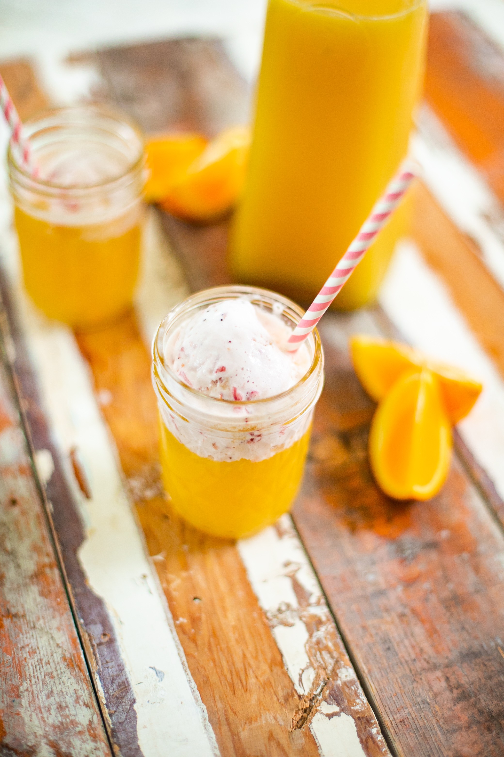 Refreshingly Easy Summer Mocktail Recipes! by popular Florida lifestyle blog, Fresh Mommy: image of a orange Summer Sorbet mocktail in mason jars with a pink and white striped straws resting a distressed wood plank counter top next to some orange slices.