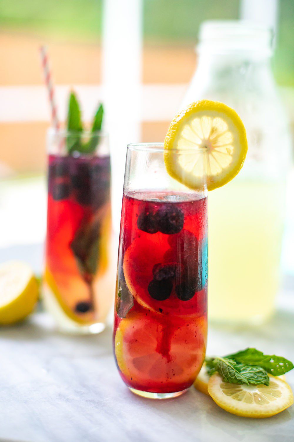 Refreshingly Easy Summer Mocktail Recipes! by popular Florida lifestyle blog, Fresh Mommy: image of Minty Blueberry Lemonade Summer Mocktail Spritzer with a pink and white stripe straw and a lemon slice on the rim of the cup and some fresh mint leaves in the top of the drink.