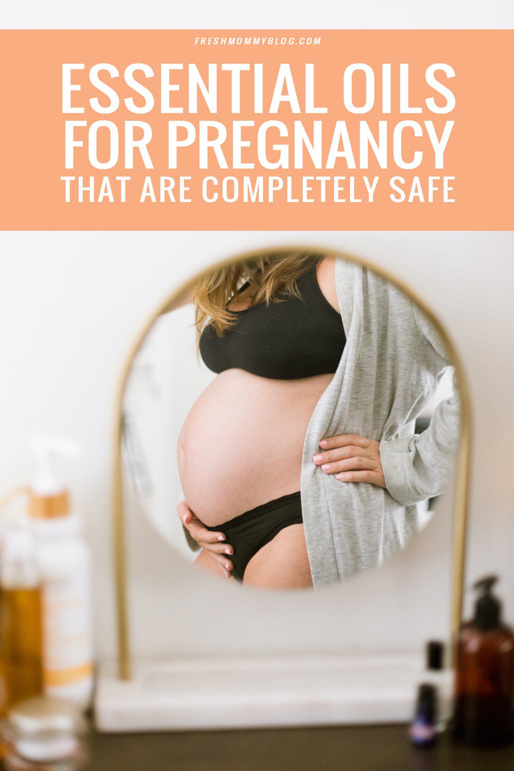 Essential Oils While Pregnant That are Completely Safe | Top 10 Essential Oils While Pregnant That are Completely Safe by popular Florida lifestyle blog, Fresh Mommy: image of woman wearing a grey robe, black sports bra, black underwear and standing in front of a mirror and holding her pregnant belly with one hand. 