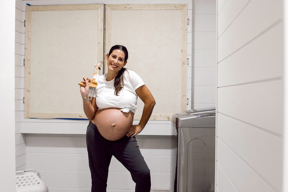 DIY for Covering your Breaker Boxes: A Faux Cabinet Tutorial by popular Florida DIY blog, Fresh Mommy: image of a pregnant woman holding a caulking gun.