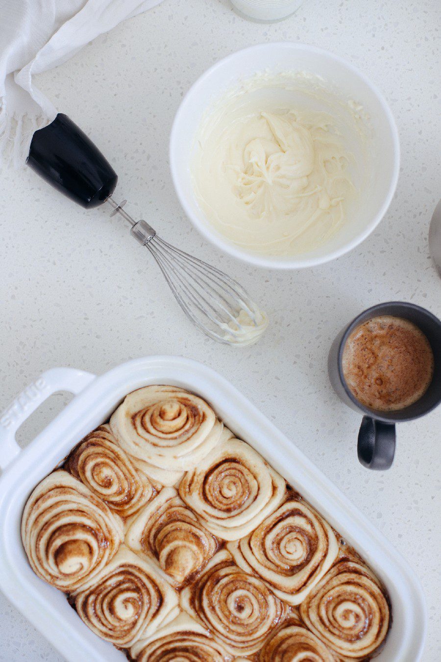 Easy bread machine cinnamon rolls dough. The best gooey sticky buns and clone of a Cinnabon roll icing! NO waiting overnight. Click for the recipe and how to video for fluffy cinnamon rolls homemade with a bread maker machine! Use all purpose flour or make them gluten free. Recipe from top Florida lifestyle blogger Tabitha Blue of Fresh Mommy Blog. | Bread Machine Cinnamon Roll Recipe by popular Florida lifestyle blog, Fresh Mommy Blog: image of cinnamon rolls in a white ceramic baking dish next to a bowl of cream cheese icing. 