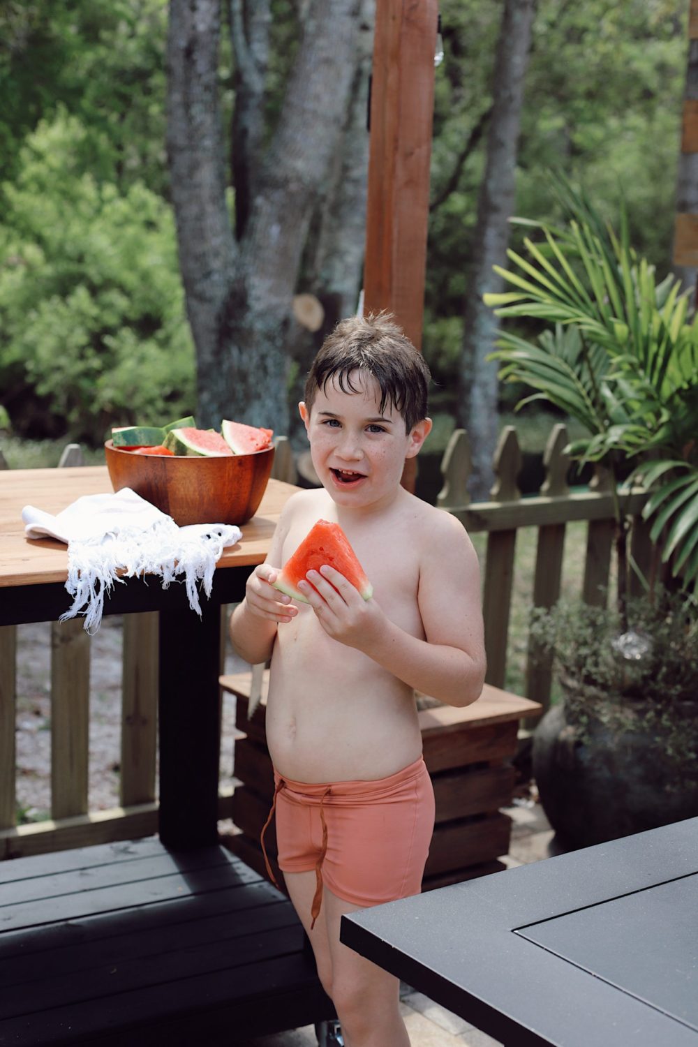 Outdoor Grill Table DIY and Plans for How To Build a Mobile Grill Cart | DIY BBQ Table by popular Florida lifestyle blog, Fresh Mommy Blog: image of a little boy wearing a orang swim suit and standing in front of a DIY BBQ table while he eats a slice of watermelon. 