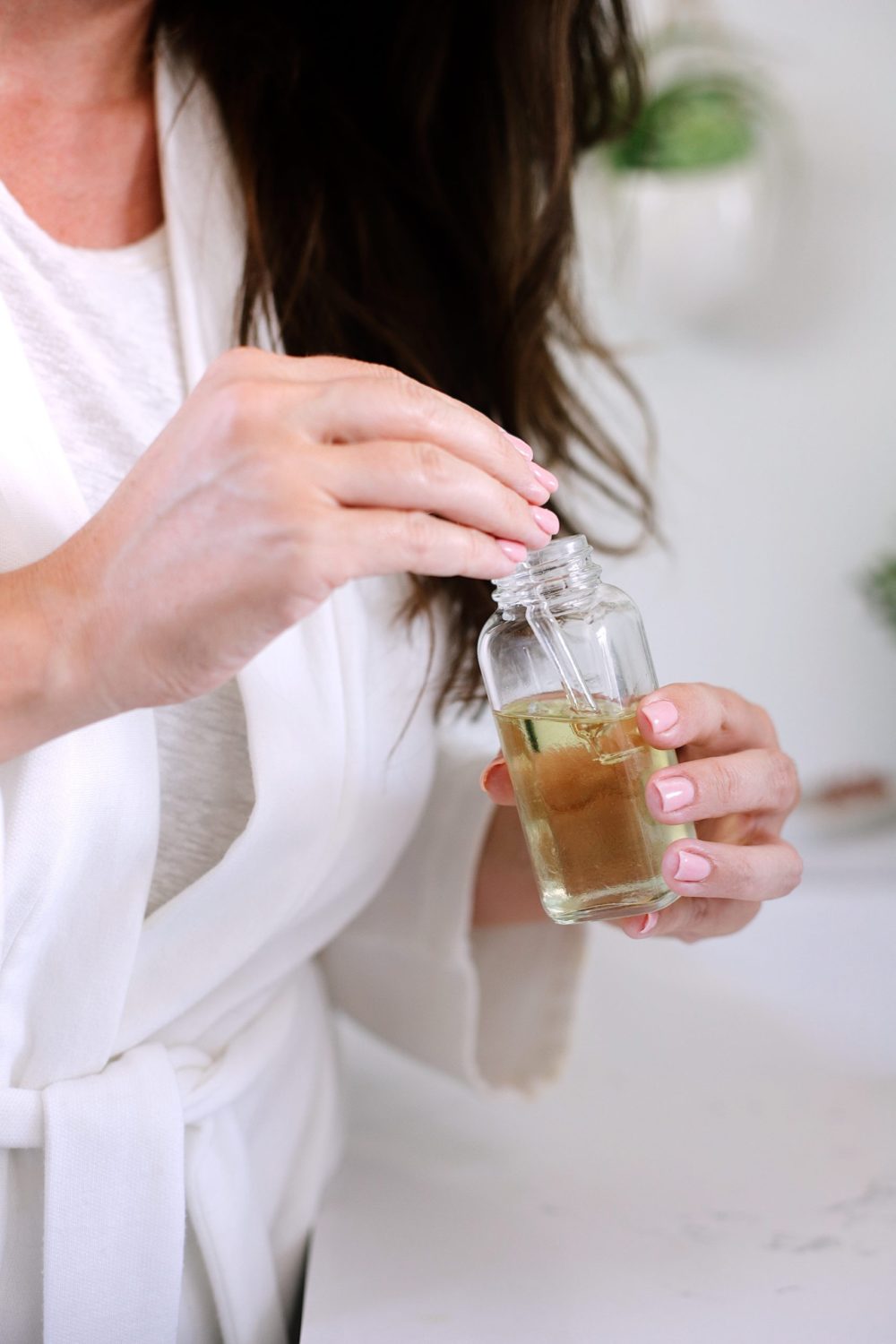 DIY Hair Growth Oil with Essential Oils Perfect for Postpartum Hair Fall. This healthy DIY scalp oil for hair growth is loaded with essential oils that boast anti-inflammatory and anti-bacterial properties that help in combating hair fall, stimulating the scalp for growth and more. |  DIY Hair Growth Oil by popular Florida beauty blog, Fresh Mommy Blog: image of a woman holding a glass bottle filled with DIY hair growth oil. 