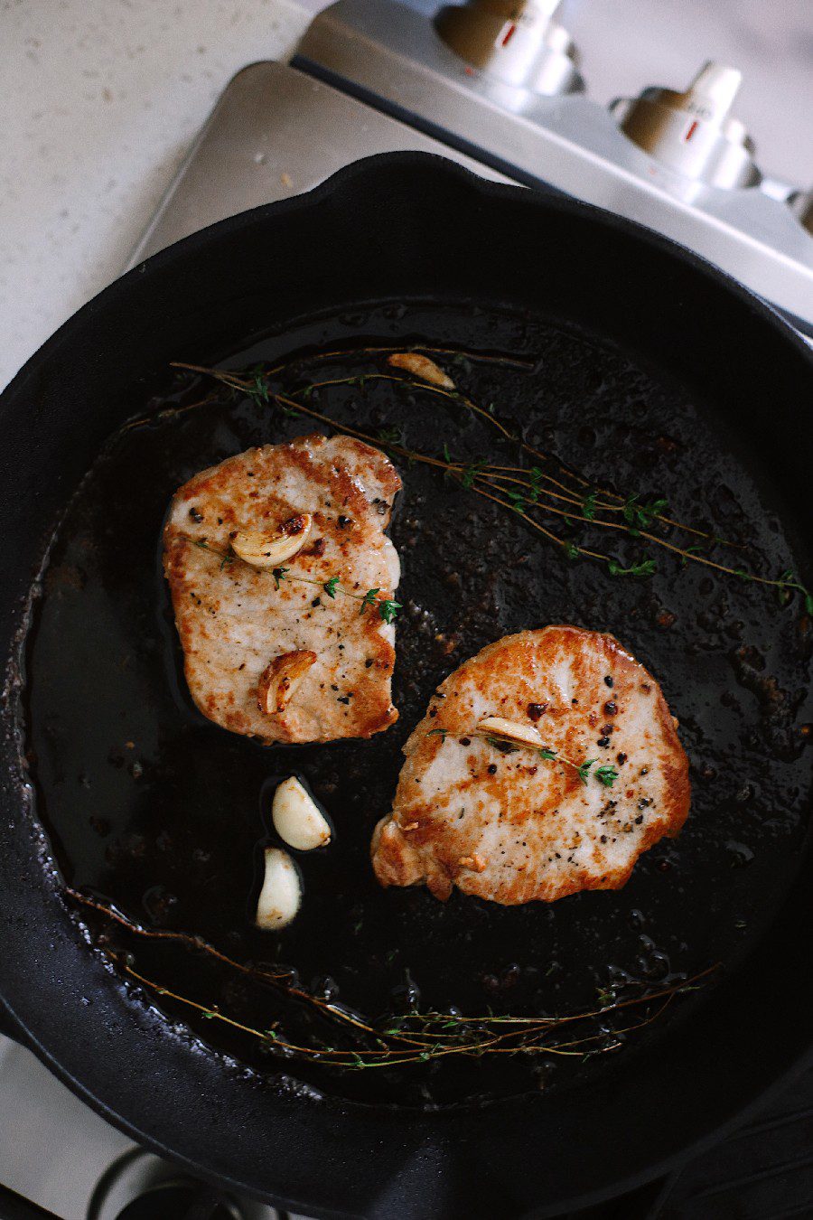 How To Cook Tender Skillet Pork Chops in the Oven What if I told you we figured out how to make sure to get those tender, juicy skillet pork chops every time, with a quick roast in the oven? Ready to say goodbye to dry, flavorless chops? These tips will have you adding tender pork chops back to your rotation. Try our pork chop recipe with browned butter garlic sauce! | Skillet Pork Chops by popular Florida lifestyle blog, Fresh Mommy Blog: image of a woman cooking skillet pork chops in her kitchen. 