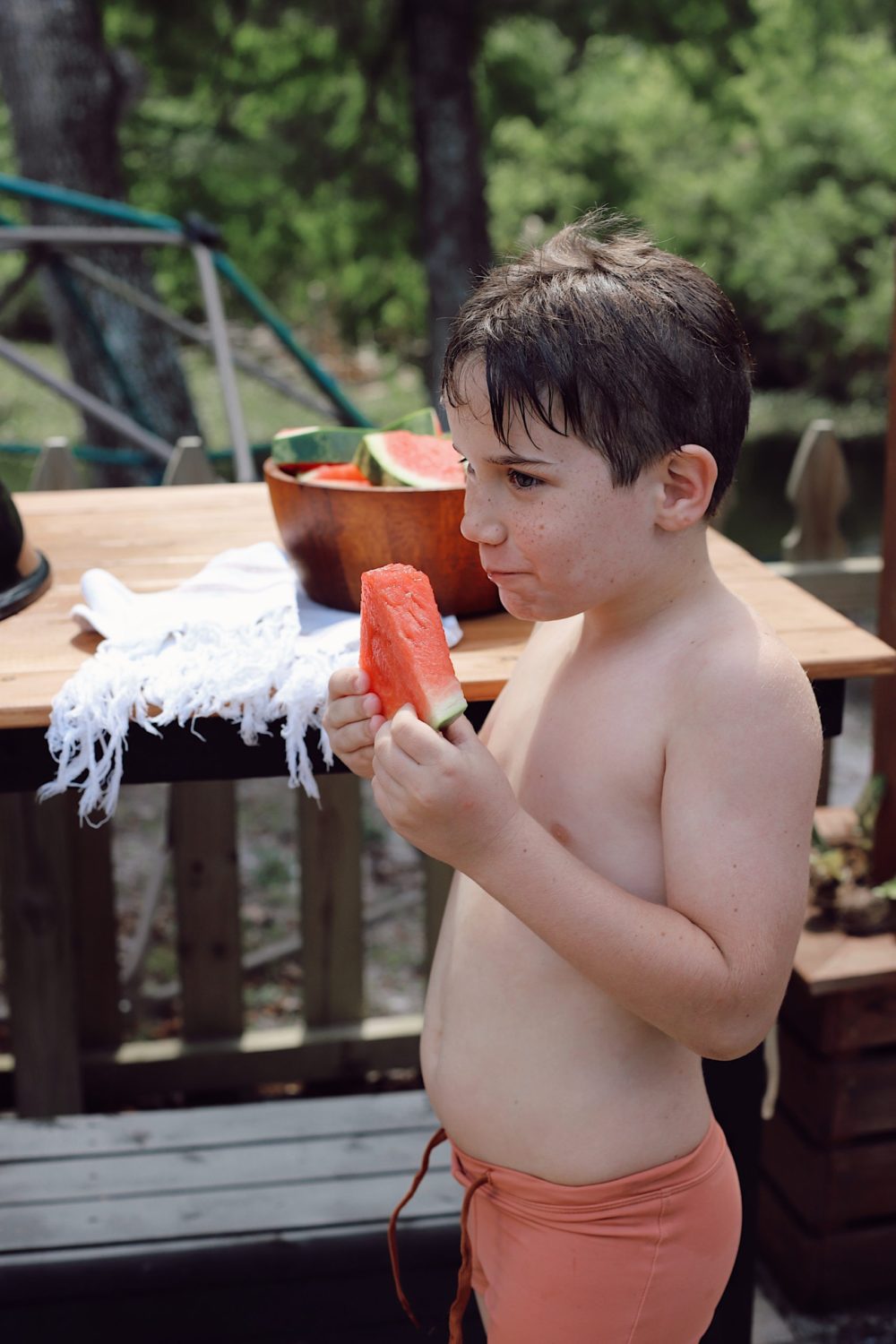 Outdoor Grill Table DIY and Plans for How To Build a Mobile Grill Cart | DIY BBQ Table by popular Florida lifestyle blog, Fresh Mommy Blog: image of a little boy wearing a orang swim suit and standing in front of a DIY BBQ table while he eats a slice of watermelon. 