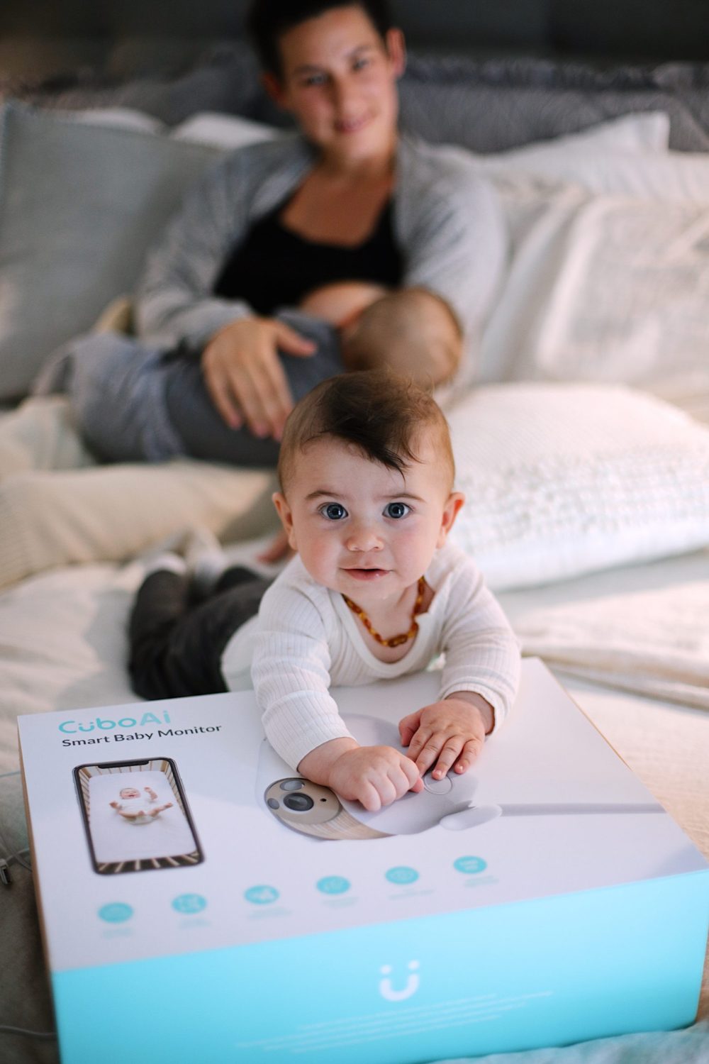 Best Baby Monitor by popular Florida motherhood blog, Fresh Mommy Blog: image of a mom holding her twin babies on a bed next to a Cubo Ai monitor box. 