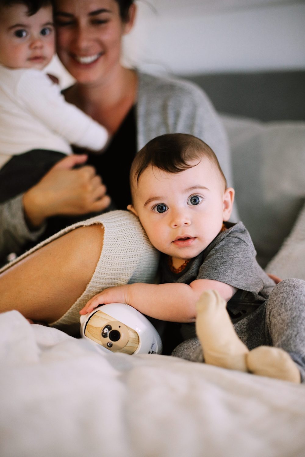 Best Baby Monitor by popular Florida motherhood blog, Fresh Mommy Blog: image of a mom holding her twin babies on a bed next to a Cubo Ai monitor. 