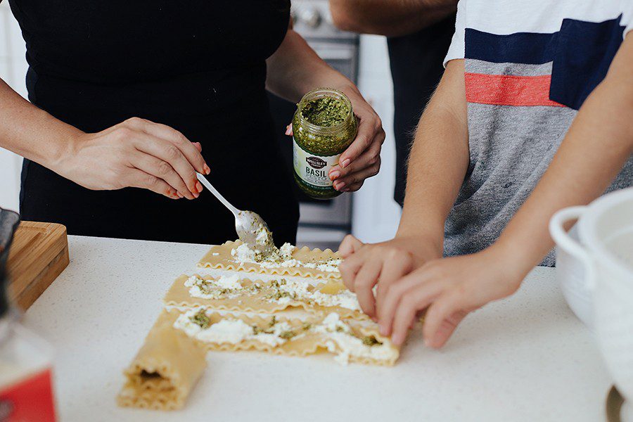 Cast Iron Lasagna by popular Florida lifestyle blog, Fresh Mommy Blog: image of a mom and her son putting ricotta cheese and pesto sauce on lasagna noodles. 
