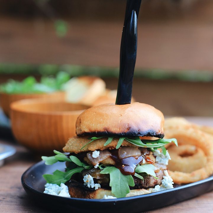 BBQ Bacon Blue Burger for a Tasty Backyard Barbecue. Not your average burger! Juicy beef burgers seasoned with a the perfect amount of spice, topped with smoked bacon jam, sweet bourbon onions, arugula, blue cheese, onion rings, BBQ sauce and a buttery grilled bun!