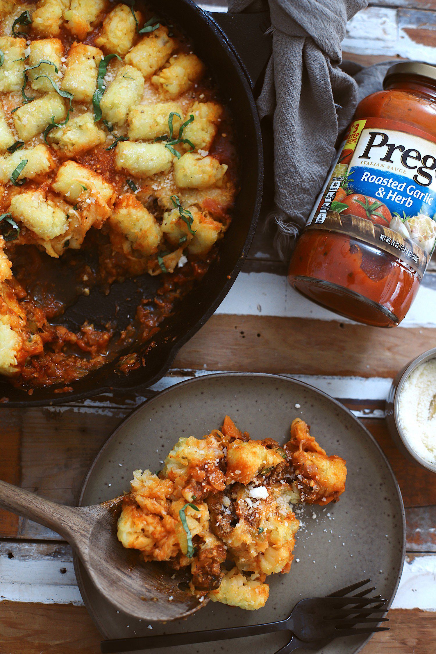This simple one skillet Bolognese Tater Tot Casserole made with Prego® is a delicious family dinner that you can make perfect any time of year with pantry staples. Think of a cross between a classic bolognese pasta and that quintessential midwest style tater tot casserole. With a cast-iron skillet, this meal boasts slowly caramelized onions in white wine, the secret vegetables of a classic bolognese, and ground beef…all cooked together in one skillet, topped with plenty of cheese, tater tots, and herbs. Simply cook the skillet in the oven to create the perfect crispy tots and cheesy, one skillet dinner! | Tater Tot Casserole by popular Florida lifestyle blog, Fresh Mommy Blog: image of a one skillet bolognese tater tot casserole in a skillet. 