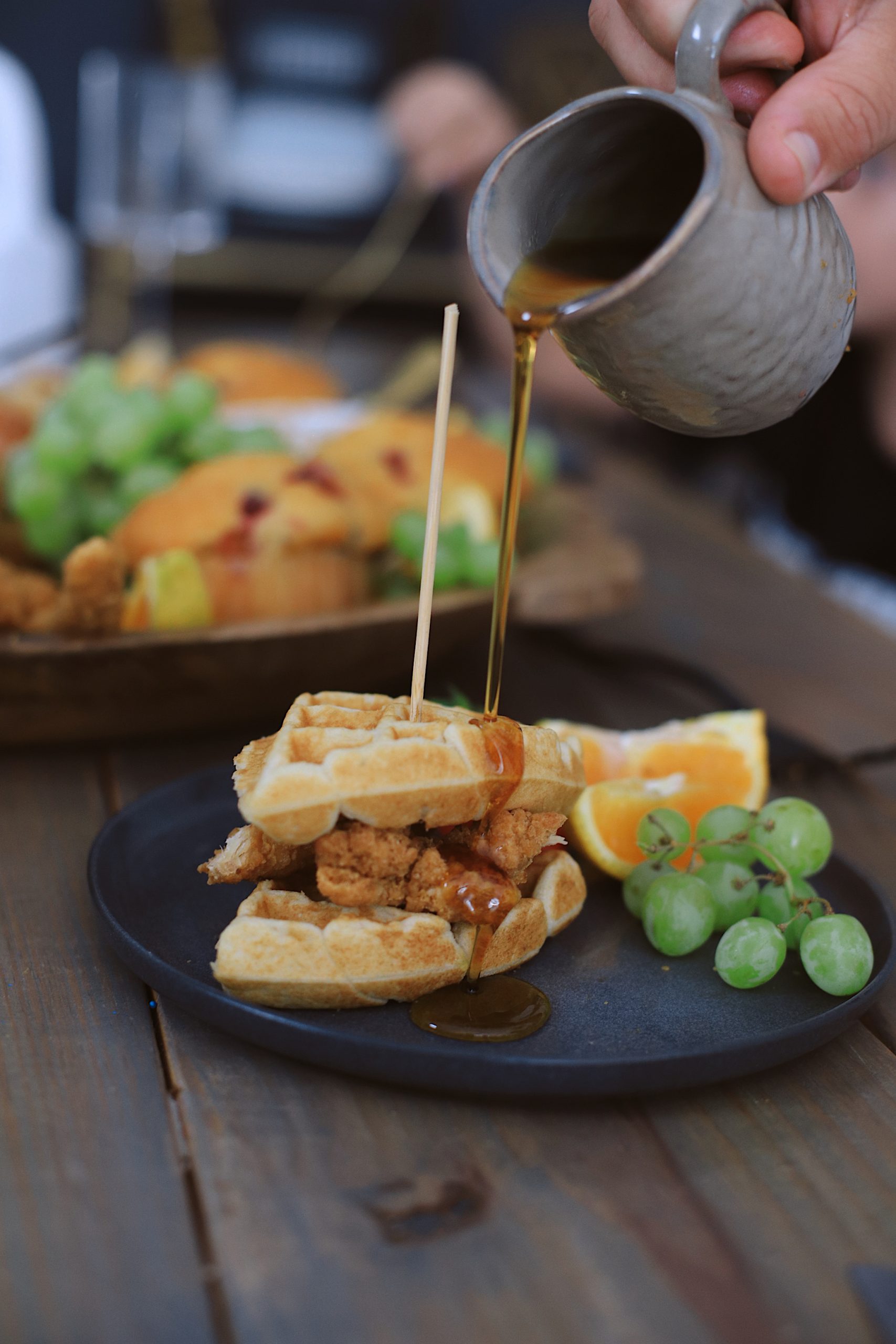 Easy Waffle Recipe for an Amazing Breakfast for Dinner Family Night - Chicken and Waffles Breakfast Board | Waffle Recipe by popular Florida lifestyle blog, Fresh Mommy Blog: image of a person pouring syrup on a chicken and waffle sandwich. 