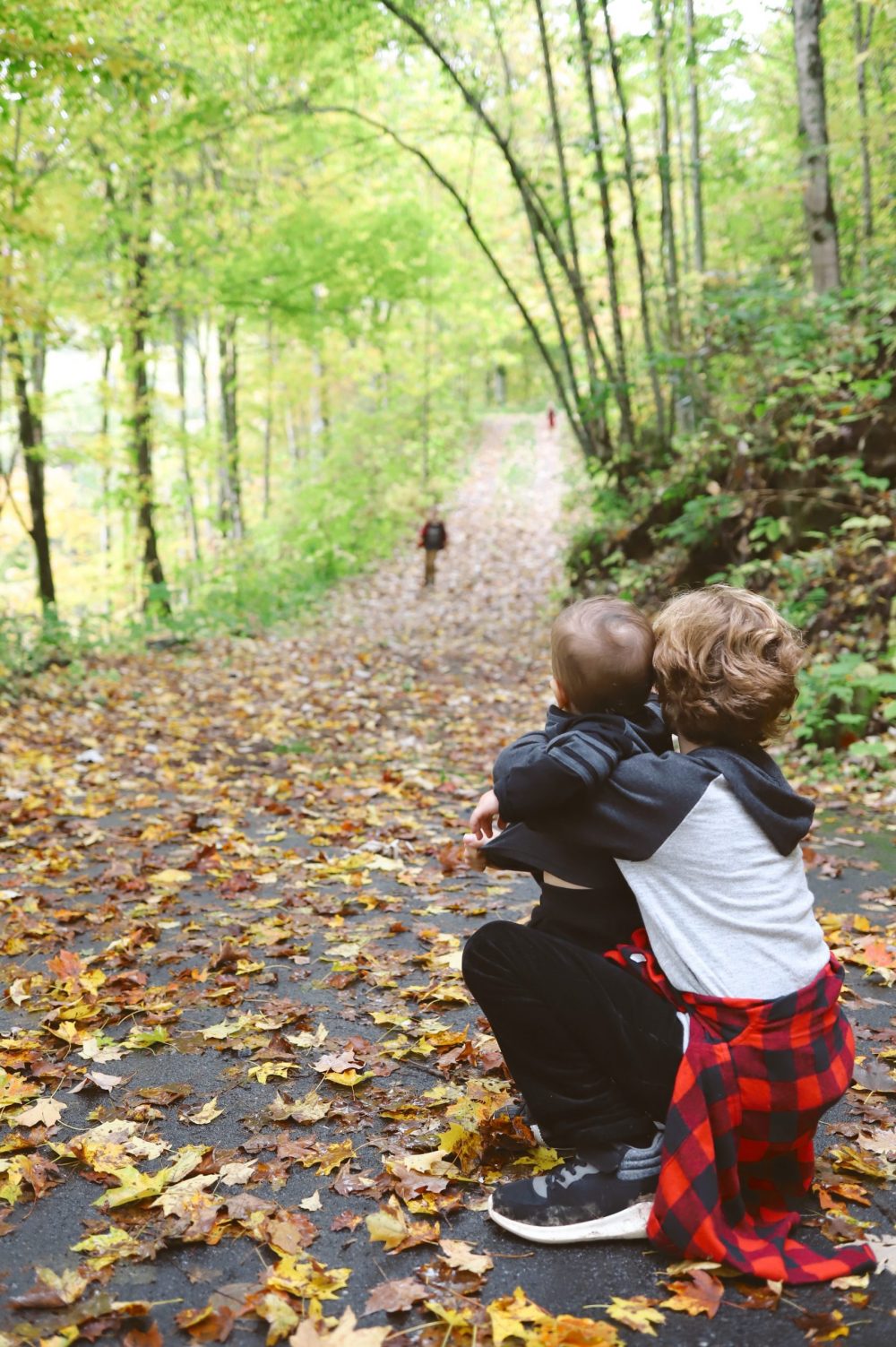 Road Trip Packing Tips by popular Florida travel blog, Fresh Mommy Blog: image of a young boy holding his baby brother on a path surrounded by trees and covered with fallen leaves. 