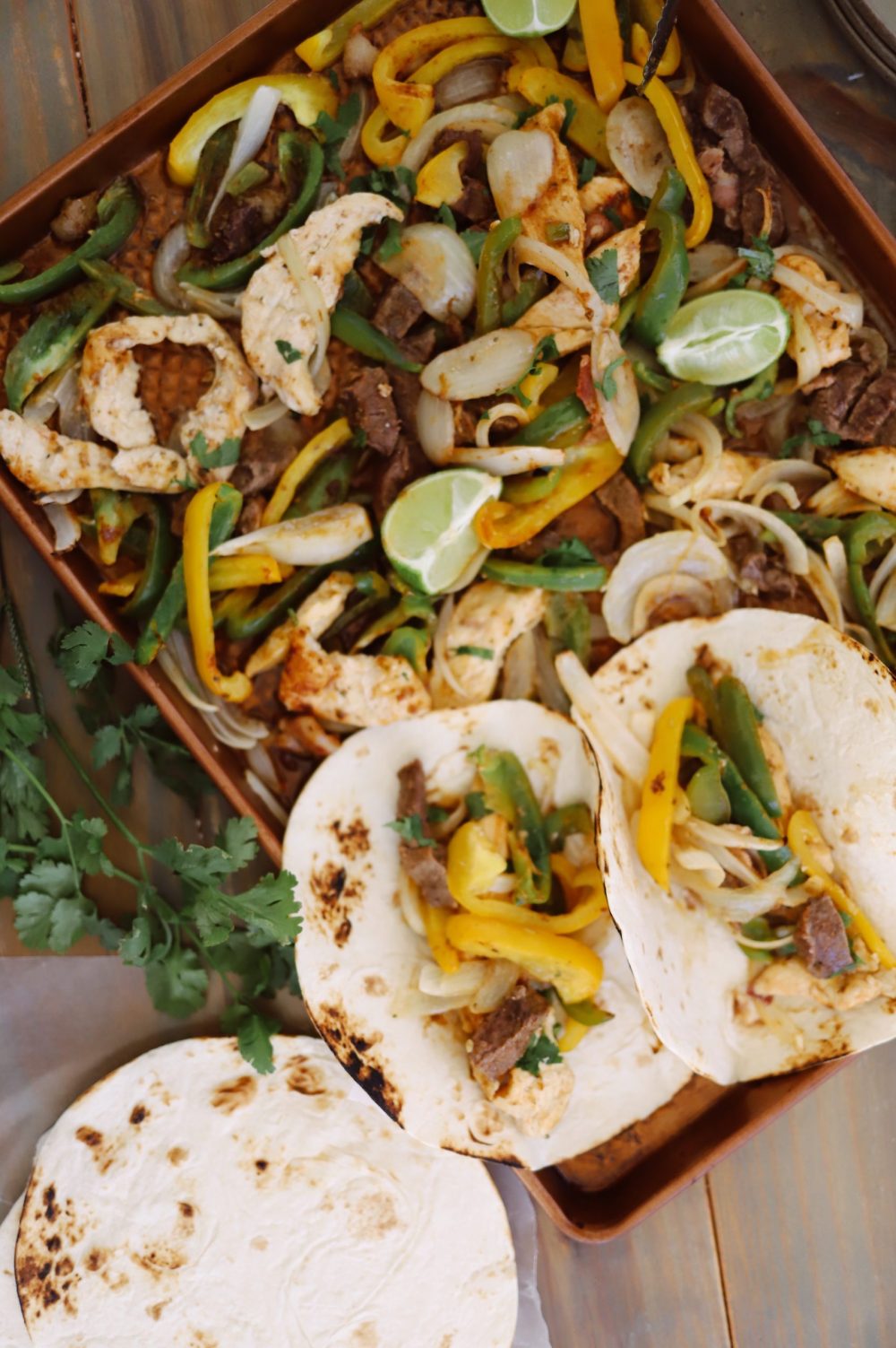 Dinner made easy and ALL IN ONE PAN with these steak and chicken sheet pan fajitas. Set it out on the table and serve with toppings to feed a big family easily!