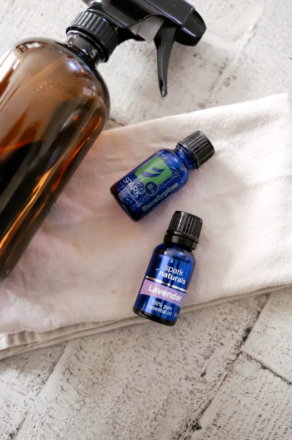 Essential Oils Safe for Dog Deodorizer Spray |Dog Deodorizer Spray by popular Florida lifestyle blog, Fresh Mommy Blog: image of a glass amber spray bottle lying next to a bottle of Spark Naturals eucalyptus oil and Spark Naturals Lavender oil. 