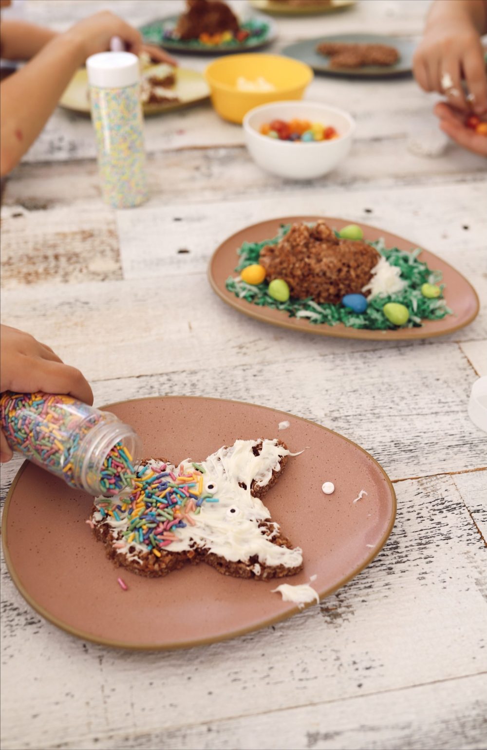 Simple Chocolate Easter Bunny Rice Krispies treats from top lifestyle blogger Tabitha Blue of Fresh Mommy Blog |Chocolate Rice Krispies Treats by popular Florida lifestyle blog, Fresh Mommy Blog: image of Easter Bunny shaped chocolate Rice Krispies treats,  a bowl of white frosting, pastel sprinkles, and white ceramic bowls filled with egg shaped jelly beans.  
