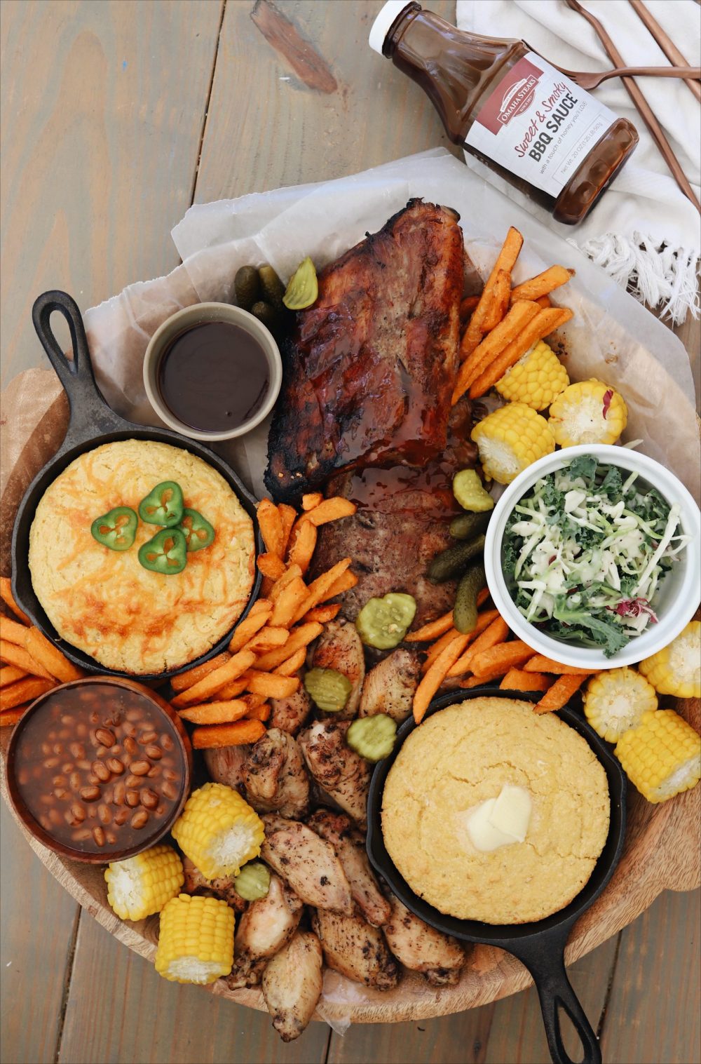 The Easiest Slow Cooker Ribs Recipe You Will Ever Make for tender fall off the bone ribs! |Slow Cooker Ribs by popular Florida lifestyle blog, Fresh Mommy Blog: image of slow cooker ribs on a wooden tray with sweet potato fries, corn on the cob, skillet corn bread, chicken wings, and a white ceramic dish of coleslaw. 