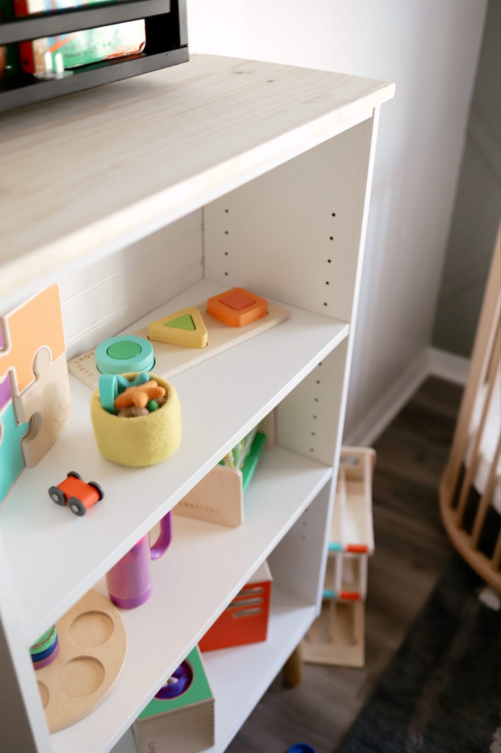 How to Upcycle your Cheap Bookcase into Stylish Mid Century Shelves: a Step by Step Tutorial featured by top FL DIY blogger, Tabitha Blue of Fresh Mommy Blog | Cheap Bookcase by poplar Florida DIY blog, Fresh Mommy Blog: image of a white bookcase filled with baby toys and books. 