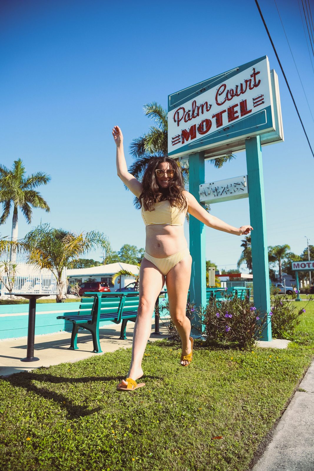 Style on a Budget: 9 Best Swimsuits for Moms |Swimsuits for Moms by popular Florida fashion blog, Fresh Mommy Blog: image of a woman standing outside at the Palm Court Motel and wearing a yellow stripe two piece swimsuit. 