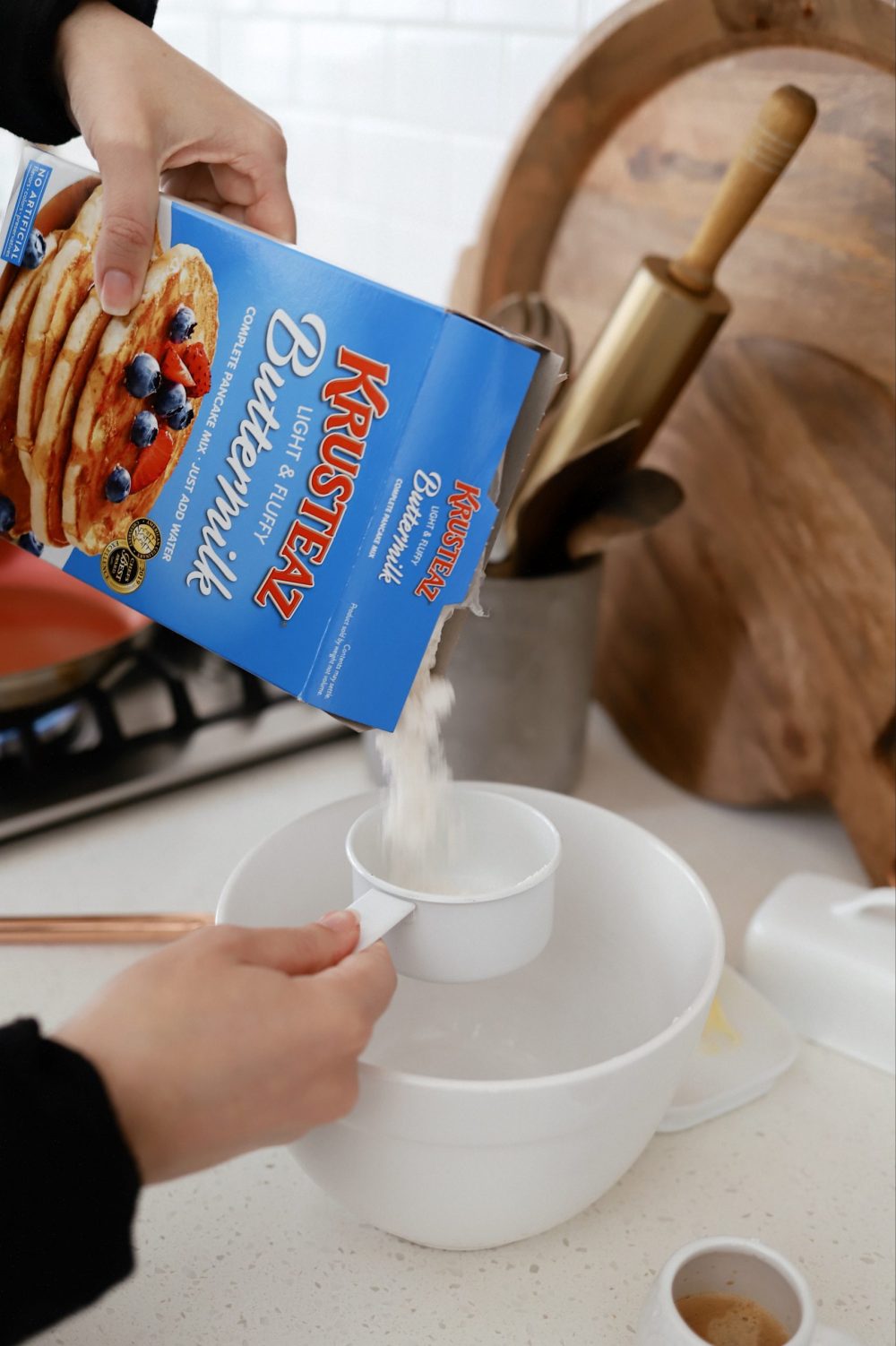 Mouthwatering Coffee Pancakes With Espresso and Vanilla Cream Whip | Coffee Pancakes by popular Florida lifestyle blog, Fresh Mommy Blog: image of a woman pouring Krusteaz buttermilk pancake mix into white measuring cup being held over a white ceramic bowl. 