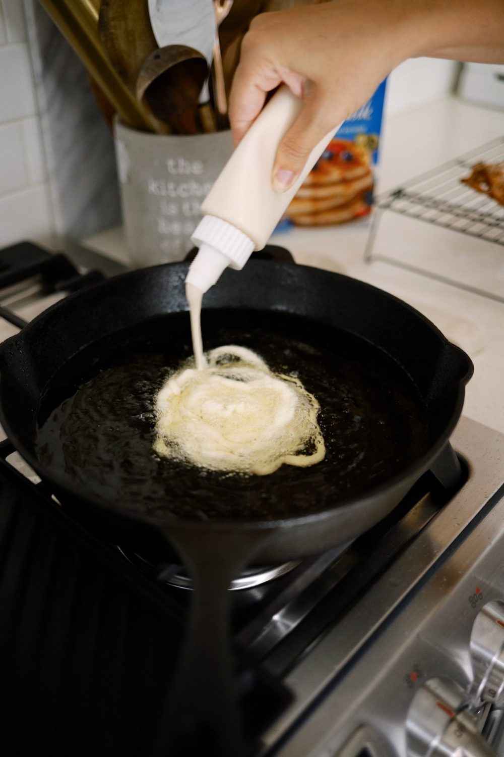 How to Make Yummy Funnel Cake From Pancake Mix at Home | Pancake Mix Funnel Cake, by popular Florida lifestyle blog, Fresh Mommy Blog: image of a woman putting pancake mix funnel cake batter in a skillet filled with oil. 