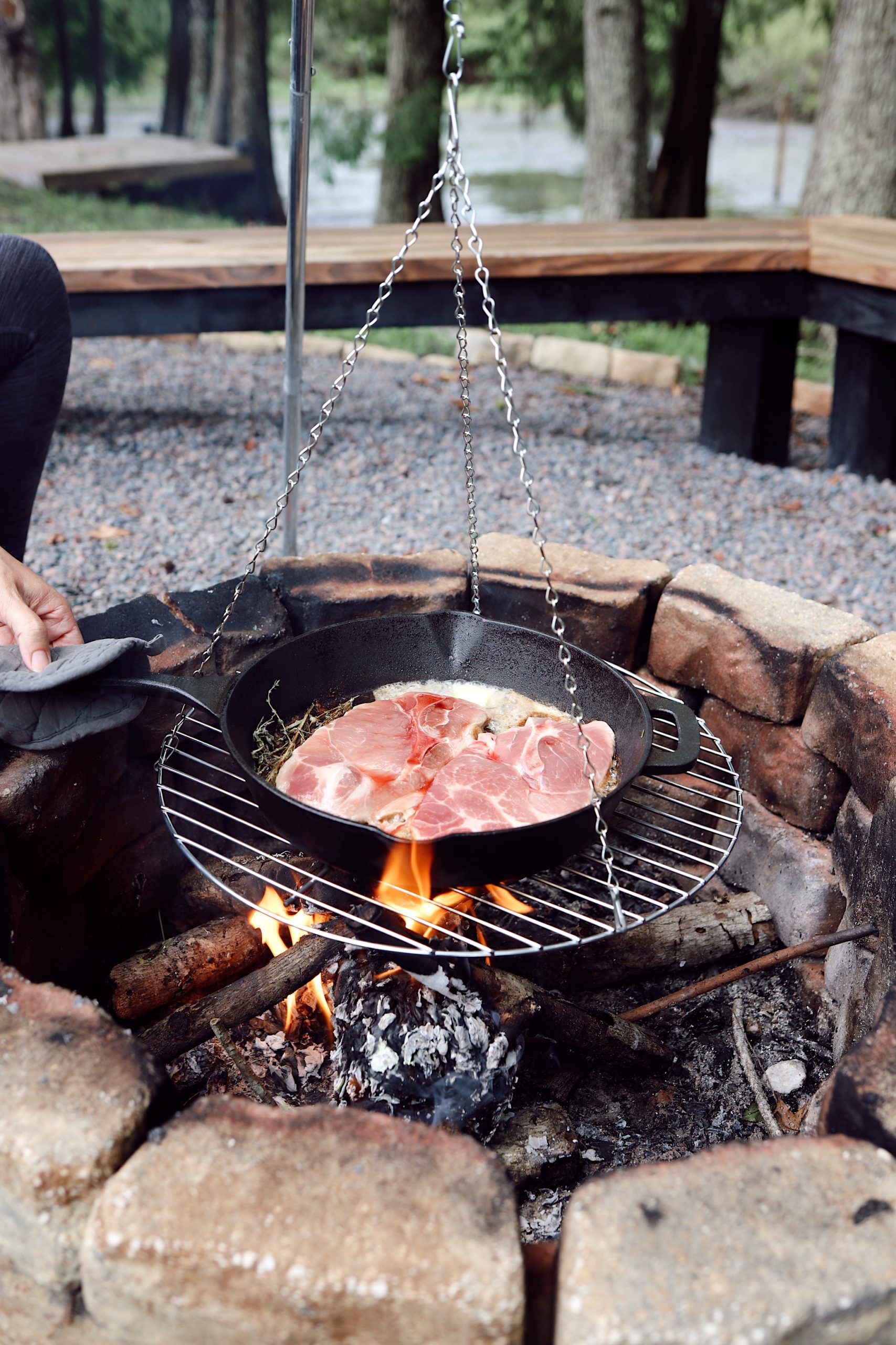 Camping Recipes - Cooking over the fire - cast iron pork loin | Grilling Season by popular Florida lifestyle blog, Fresh Mommy Blog: image of a woman cooking pork loin in a cast iron skillet over a camp fire. 